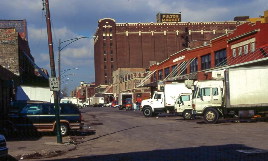 Fulton Street at Peoria Street in 2002: delivery trucks and pickups parked outside brick loading docks, beneath the old Fulton Market cold-storage building with its rooftop sign.