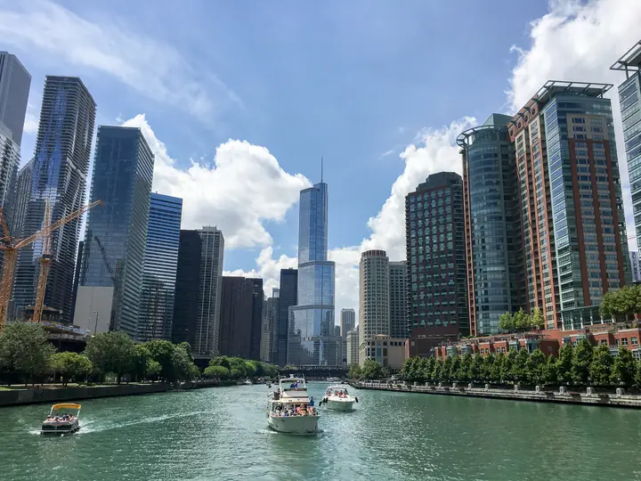 Boats on the main branch of the Chicago River, lined with glass towers and riverside trees.