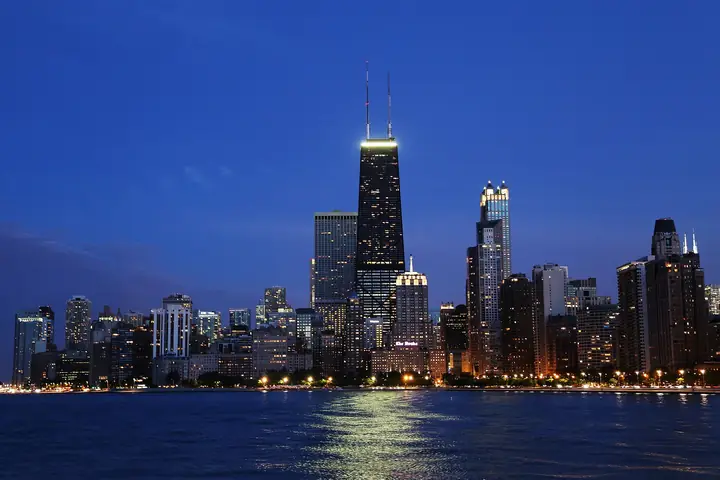 The Chicago skyline at dusk from across the water at North Avenue Beach, with the John Hancock Center lit up and reflections on Lake Michigan.