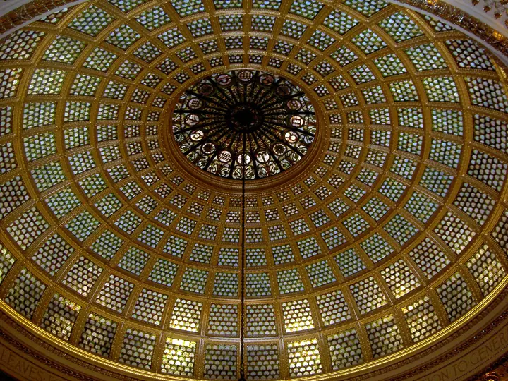 Looking up into the Tiffany glass dome of the Chicago Cultural Center, a mosaic of thousands of glass pieces glowing gold and green.