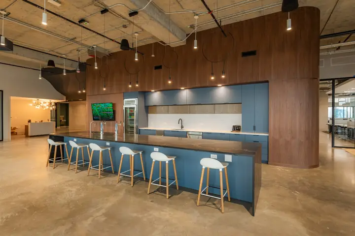 A long kitchen island with blue cabinets, walnut paneling and white bar stools in Portal's open common area.