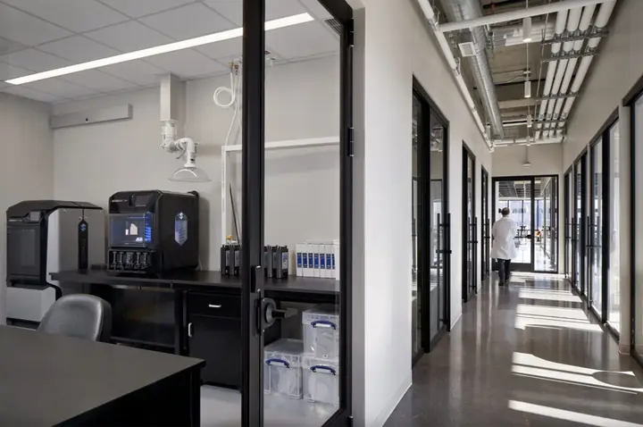 A corridor of glass-fronted private lab suites with benchtop equipment visible through the glass.