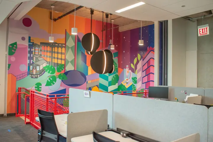 A vivid mural of stylized Chicago buildings and plants in pink, teal and orange, above work pods and a red spiral staircase between floors.