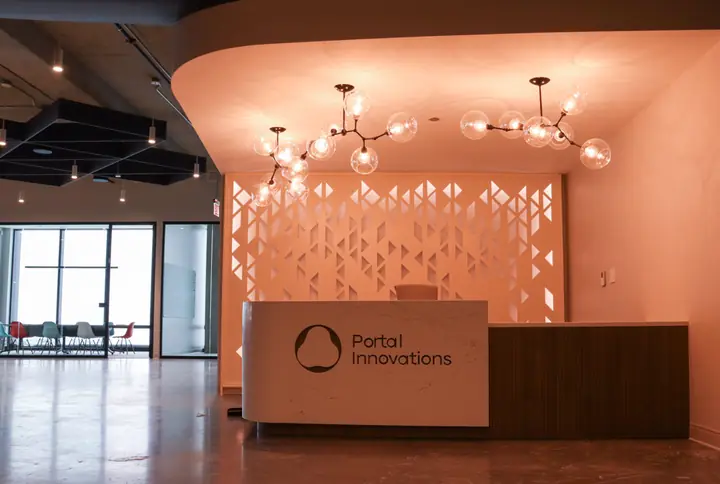 Portal Innovations' reception desk in a warm, coral-lit lobby, with glass-globe chandeliers and a patterned screen behind the desk.