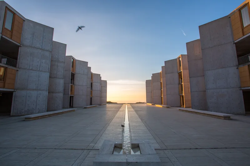 Sunset over the Pacific at the end of the Salk Institute courtyard, the thin water channel running down the center of the plaza between the concrete towers.